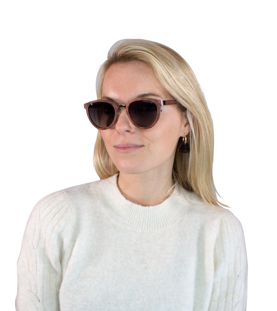 Closeup of female model in brown wood sunglasses with dark non-mirror lenses, gold tone accents at bridge and temples