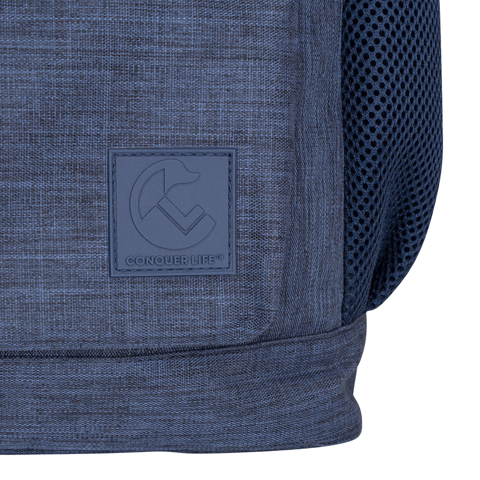 Closeup front view of navy blue poly-fabric backpack, lower right corner, blue plastic Conquer Life logo patch, 1" square