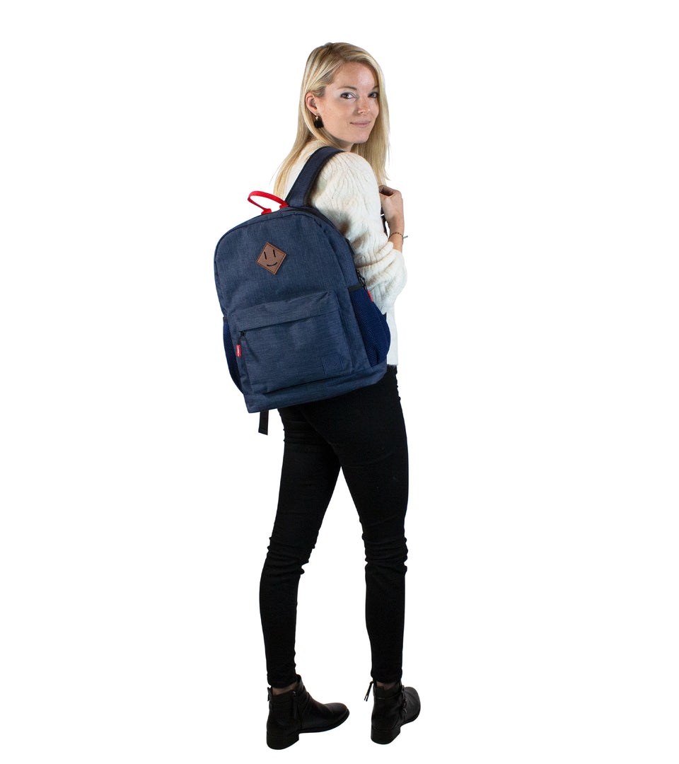 Rear view of standing female model wearing navy blue poly-fabric backpack strapped over 1 shoulder, turning face to camera
