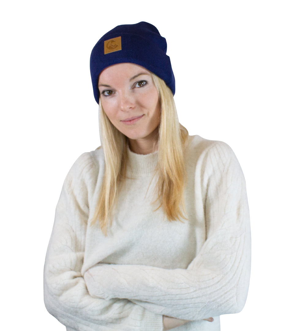Front, waist-up view of female model with folded arms, in navy blue, acrylic knit beanie: faux-leather patch at cuff center