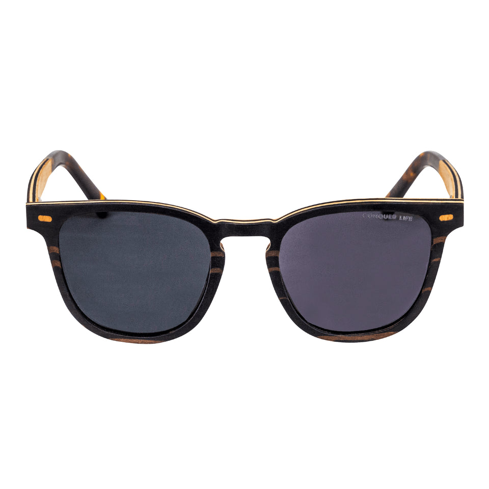 Front of brown striped wood wayfarer sunglasses: gold corner accents, tortoiseshell acetate arm tips, dark non-mirror lenses