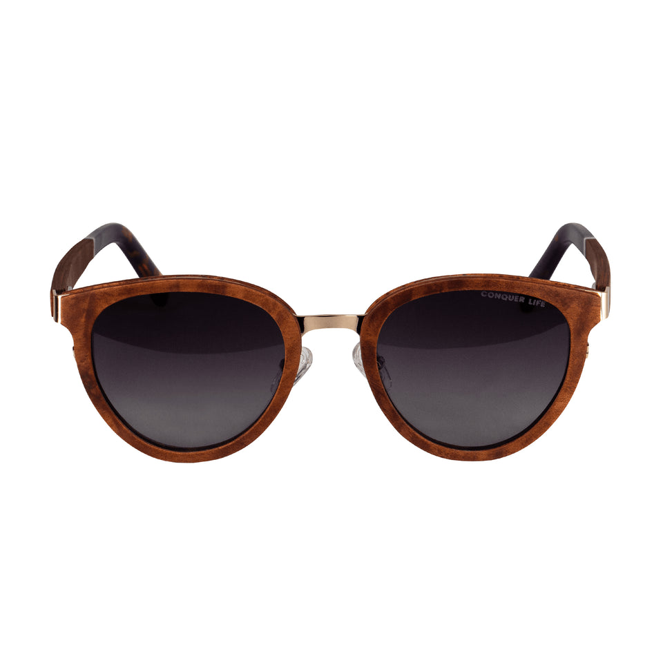 Front sunglasses with wood frame, gold tone metal bridge, dark non-mirror lenses with Conquer Life in corner