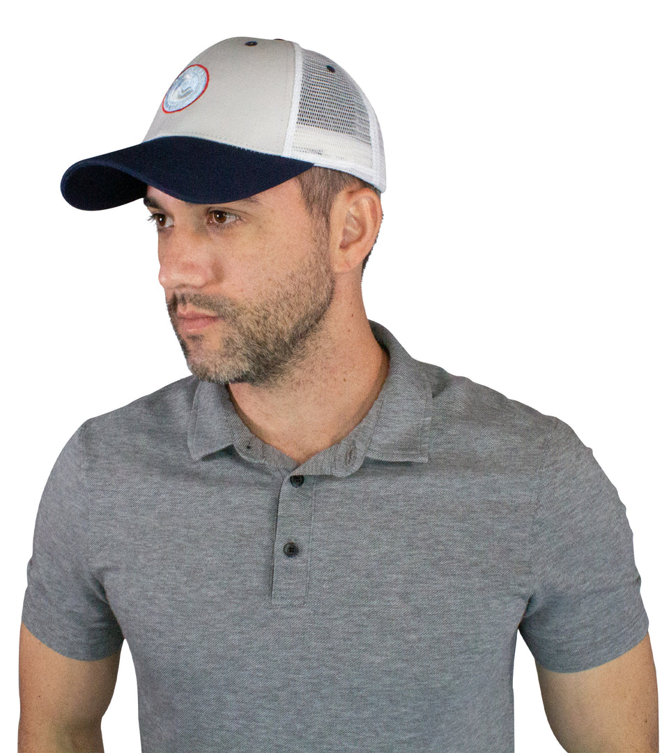 Waist up 3/4 profile of male model in trucker hat with blue bill & circular, red, white, & light blue patch & white mesh back