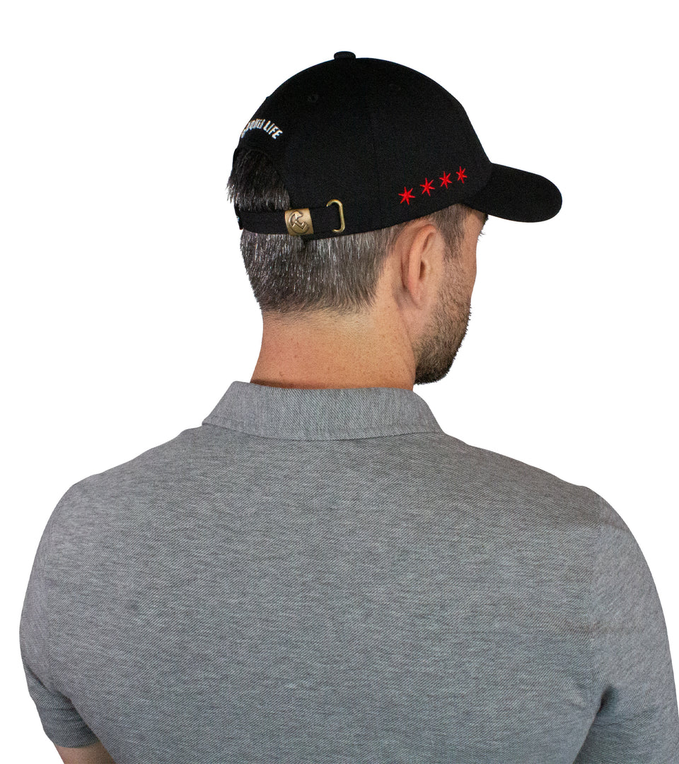 3/4 rear view of male model in black cotton-nylon cap: bronze hinge and white Conquer Life text at back and red stars on side